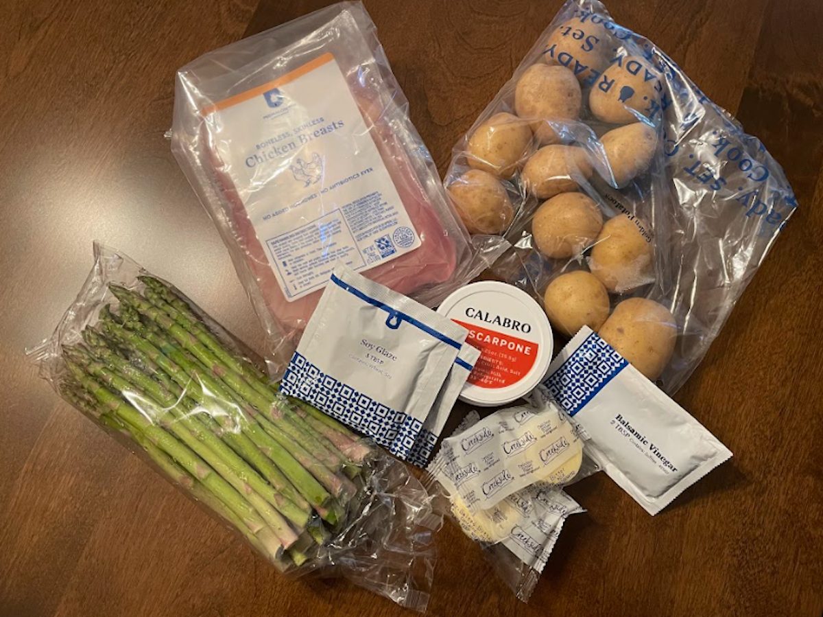 Bagged asparagus, potatoes, and chicken breasts with packets of seasonings and other ingredients