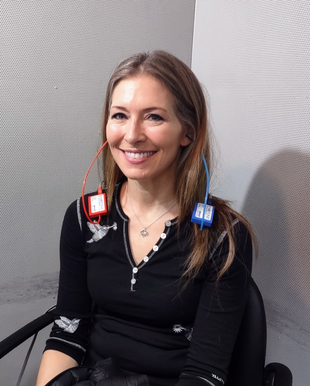 A person receiving a hearing exam at an audiologist. Two devices are in her ears during testing to help determine her level of hearing loss.