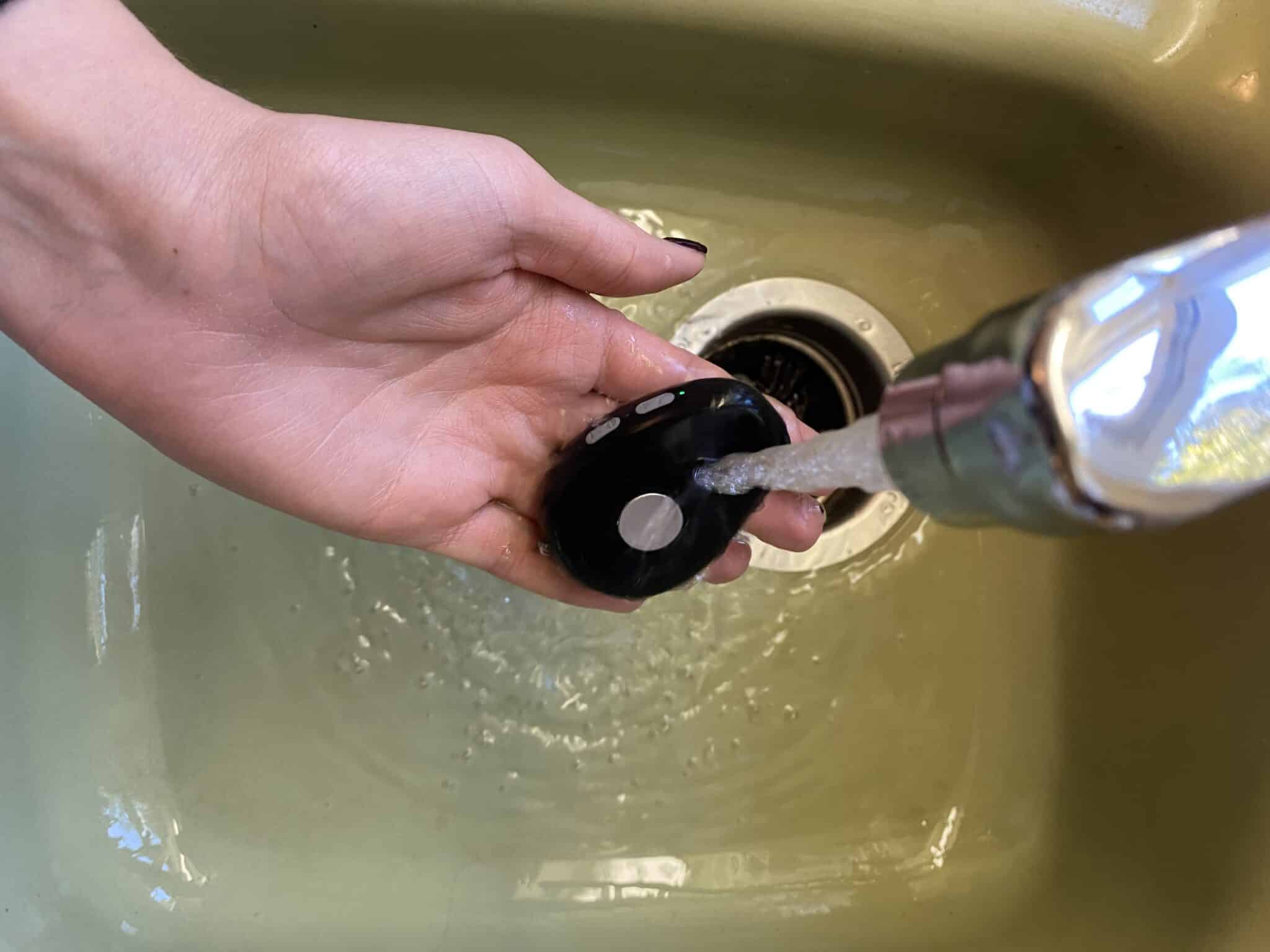 Mobile medical alert system under a stream of faucet water for a durability test.