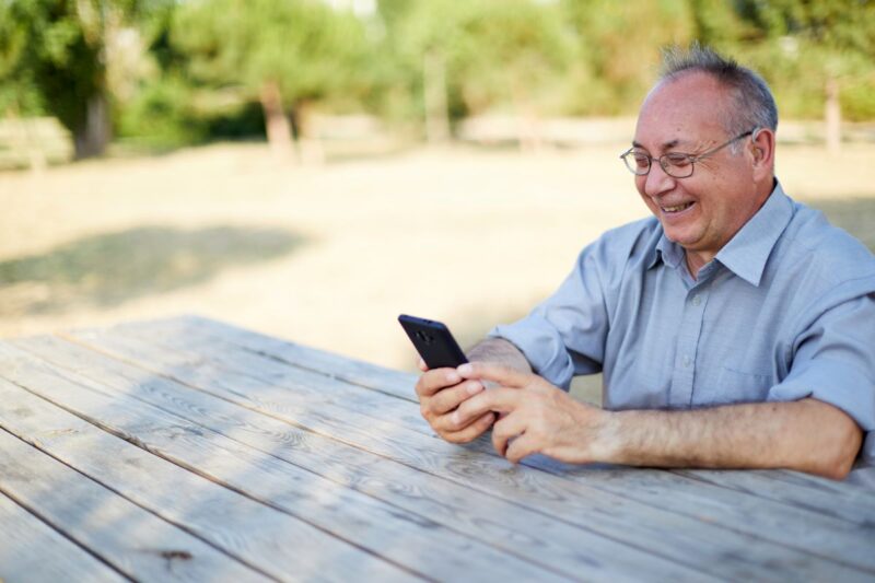 Older adult man wearing bluetooth hearing aids and using smartphone outside
