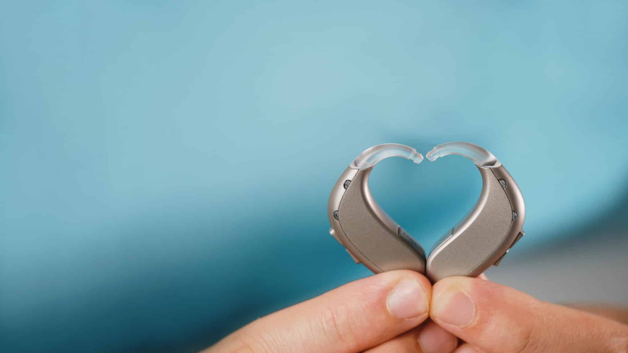 Fingers pressing a pair of hearing aids together in the shape of a heart