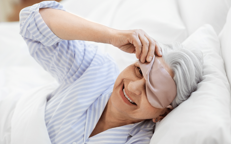 Woman waking from sleep and removing her eye mask.