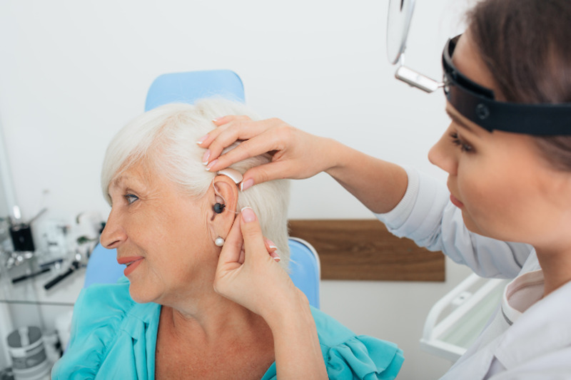 Audiologist fitting a senior woman for hearing aids