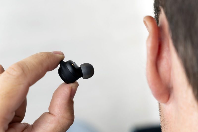 Man prepares to insert modern hearing aid into left ear