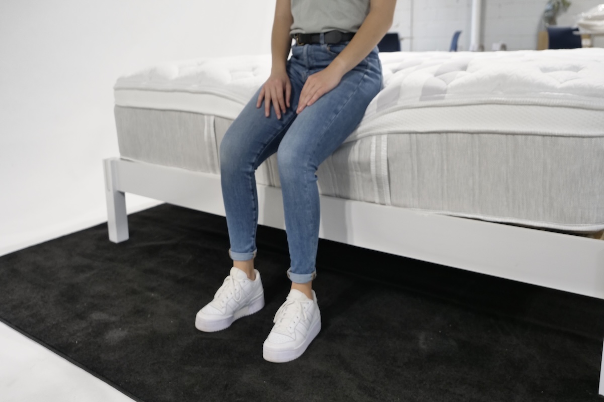 Woman sitting on the edge of a Leesa Sapira Chill Hybrid mattress.
