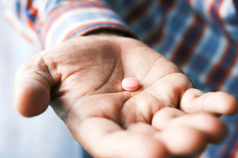 Round pink tablet resting on a man’s palm