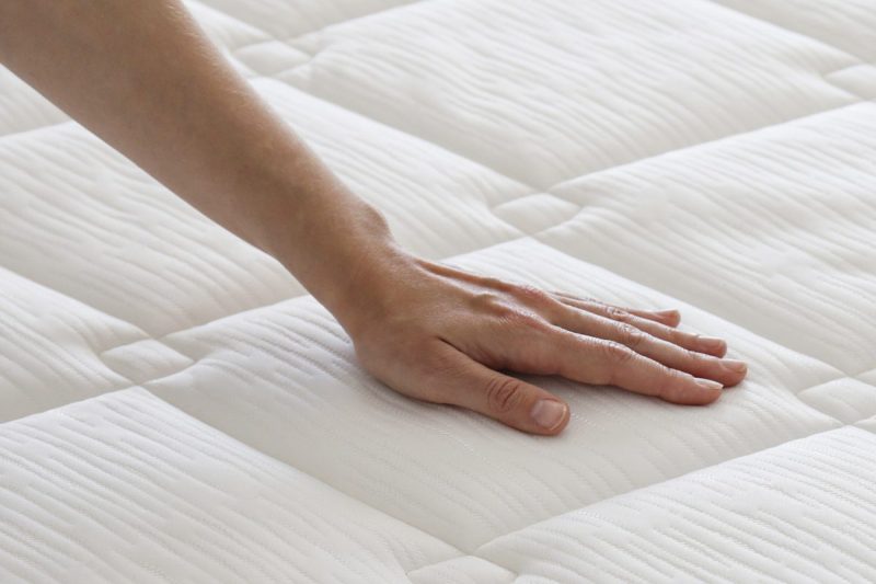 a person runs a hand over a white, freshly made bed