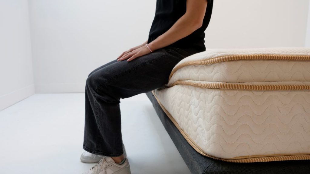 Person sitting on the side of a mattress to test edge support