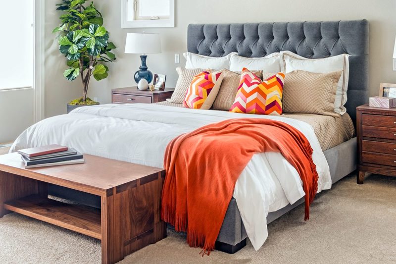Bed made with white comforter along with orange pillows and throw blanket