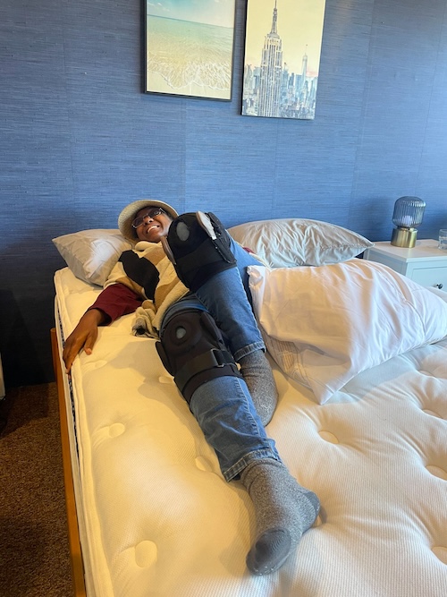 A smiling woman wearing knee braces lies on a WinkBed mattress to test it for comfort.