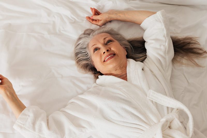 Smiling woman lying in bed in a white bathrobe