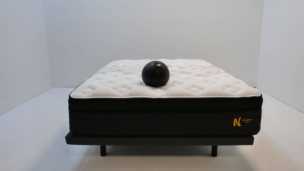 A queen-sized Nolah Evolution mattress with a weighted ball resting on top.