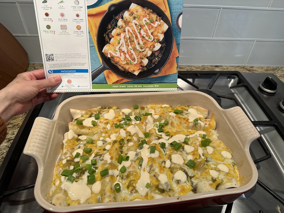 Cooked enchiladas in a pan with a hand holding the recipe card next to the pan 
