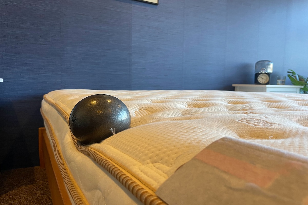 A black 10-pound ball rests on the edge of the Saatva Classic mattress, showcasing the bed’s impressive edge support.

