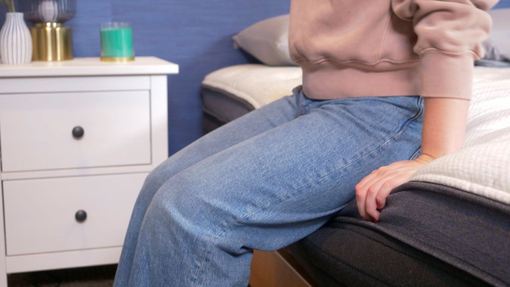 Person sitting on the edge of the Helix Midnight Luxe mattress.