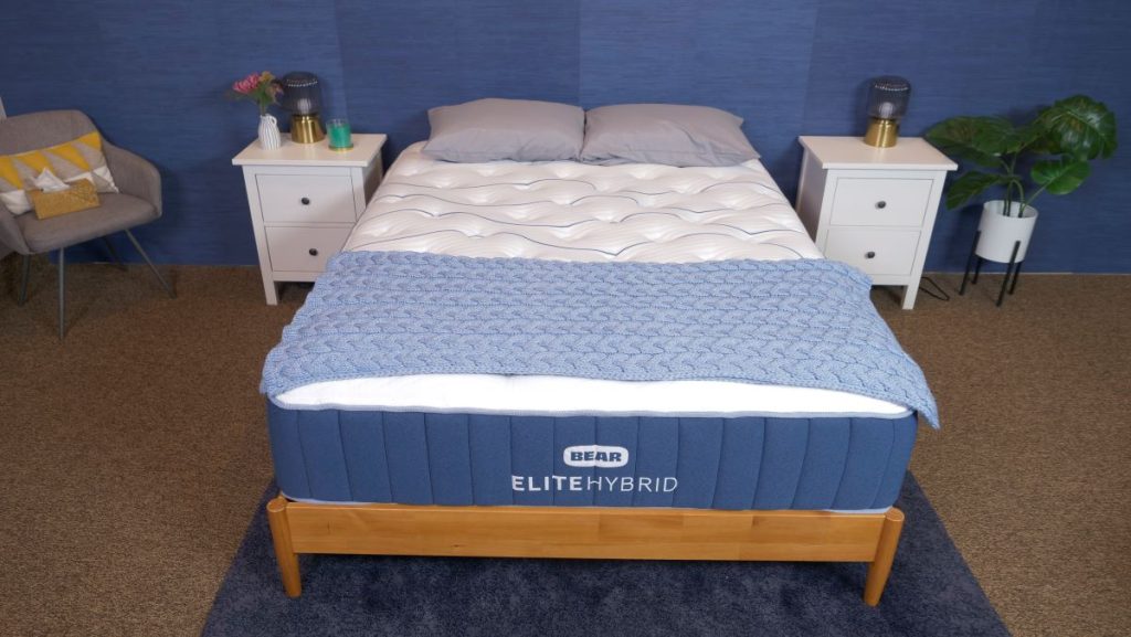 Bear Elite Hybrid on a wooden bed frame with a blue blanket.