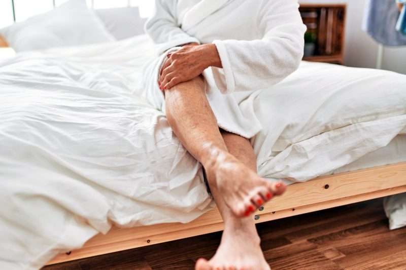 woman holds knee in pain as she exits her bed