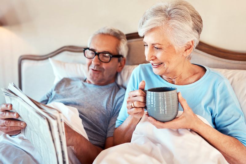 man and woman smile while lying in bed and reading