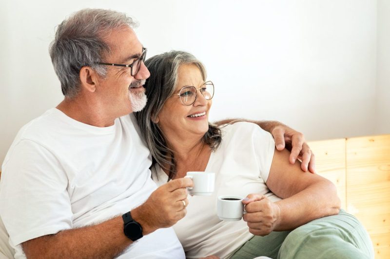 man and woman rest on bed while drinking coffee