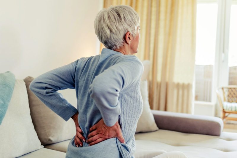 woman clutches back in pain while sitting up in bed