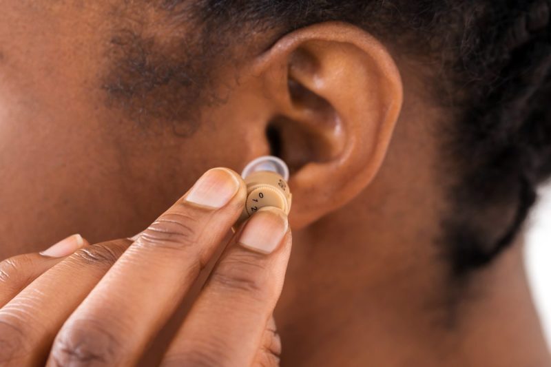 woman inserts hearing aid into her left ear