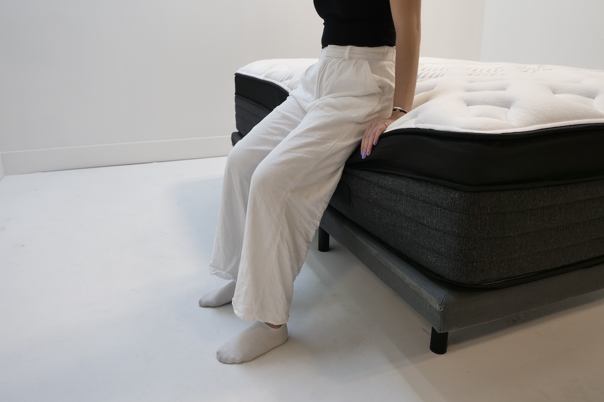 A person sits on the very edge of the Nolah Evolution mattress.