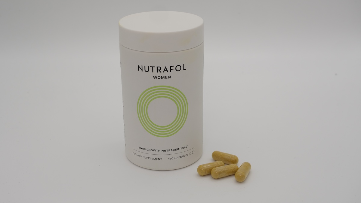 Container of a Nutrafol hair loss supplement for women with four capsules next to it.