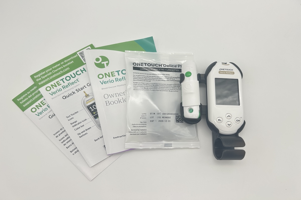 A OneTouch Verio Reflect glucose monitor, the user manuals, and a package of lancets on a white table.