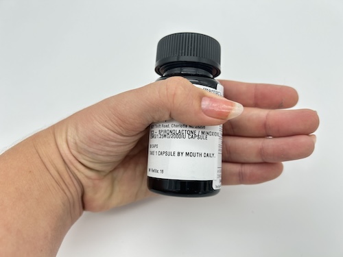 A person's hand holding a prescription bottle of spironolactone