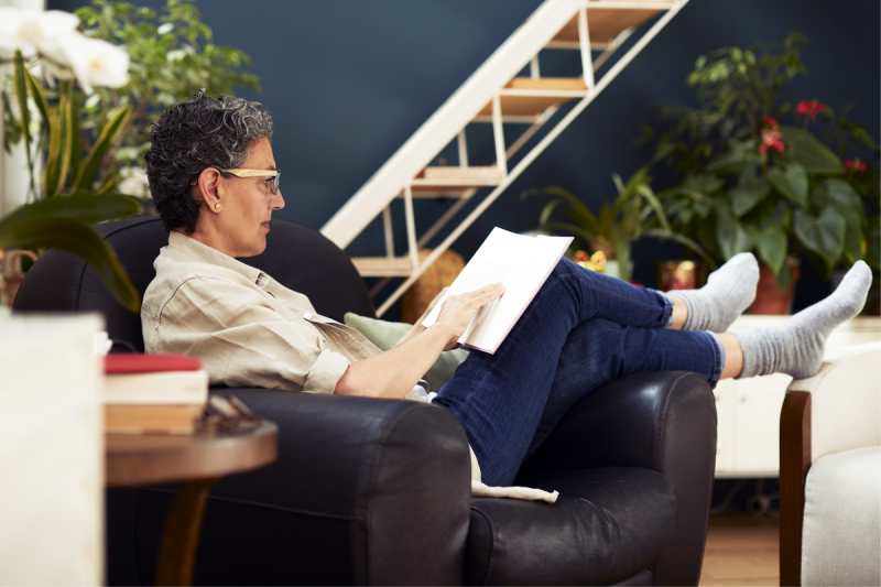 older adult woman relaxes in recliner while reading a book